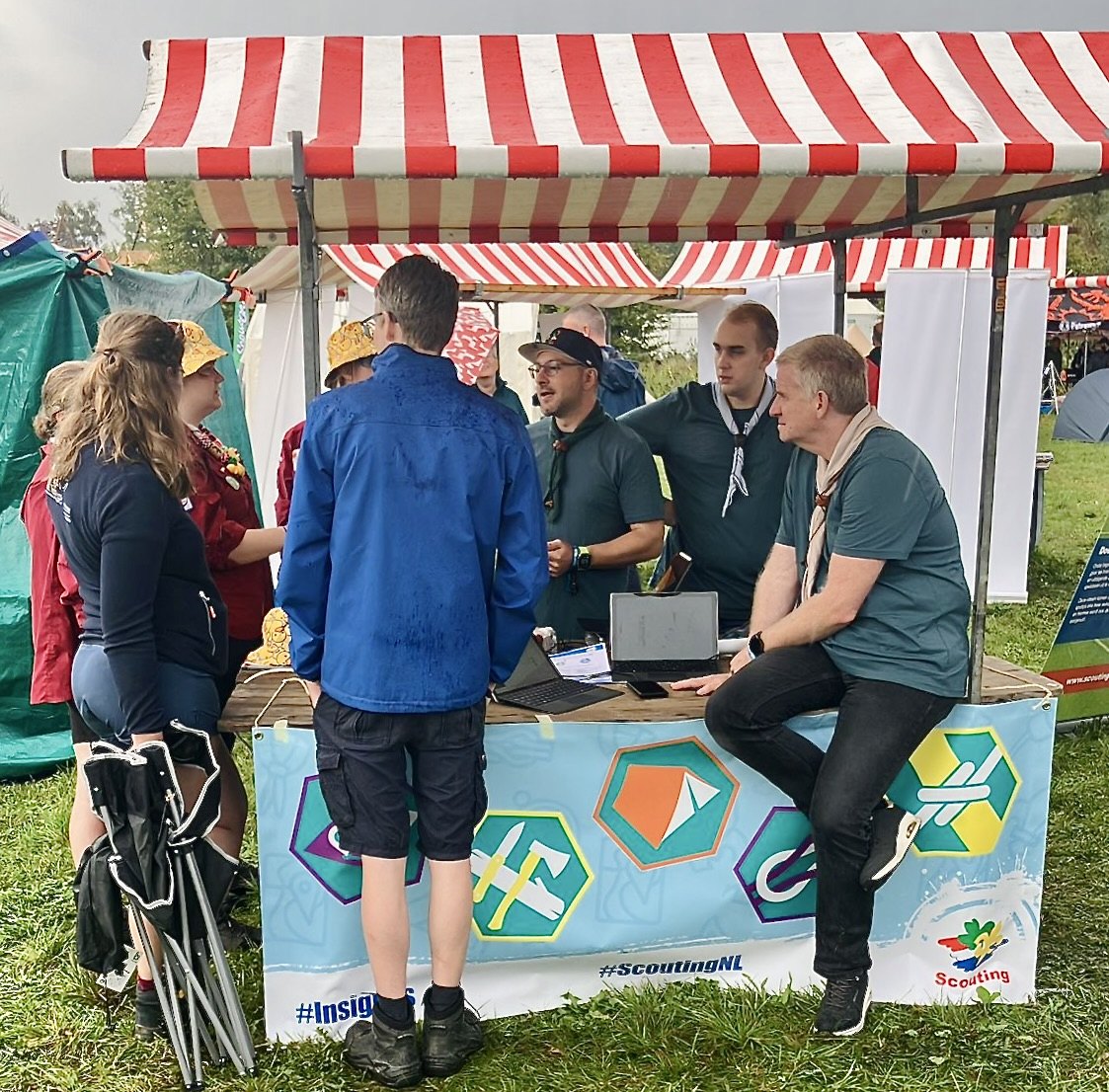 Leiding in gesprek bij de ScoutBadger-stand, met een banner vol insignes